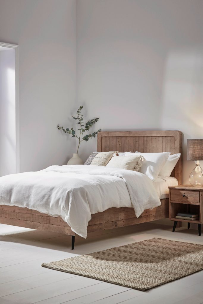 a guest bedroom with a wooden bed and white bedding with a natural jute rug on the floor