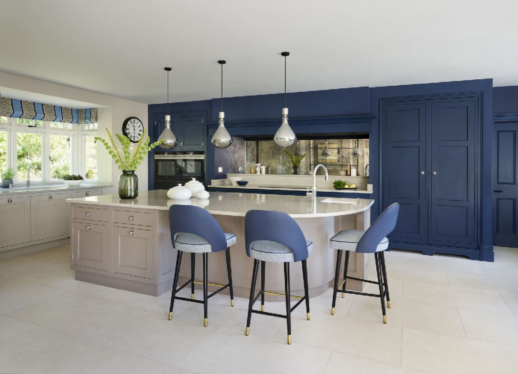 a neutral-coloured island with three silver pendant lights above it and navy bar stools around it