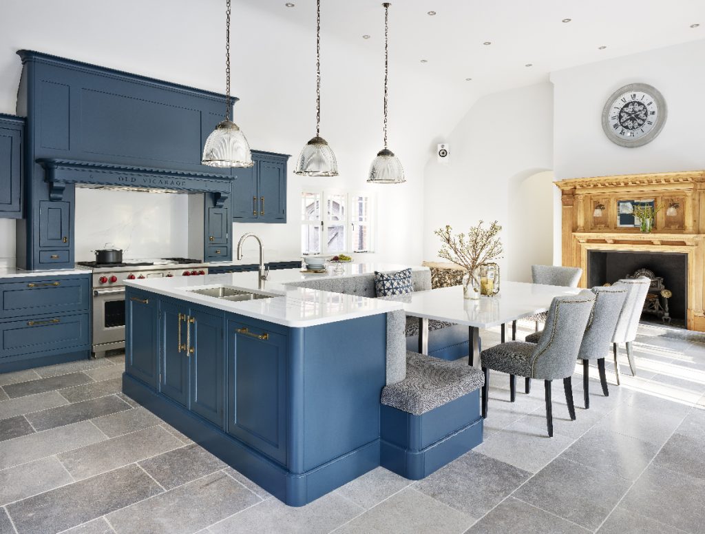 a blue shaker-style kitchen with three pendant lights above an island with a built-in seating area