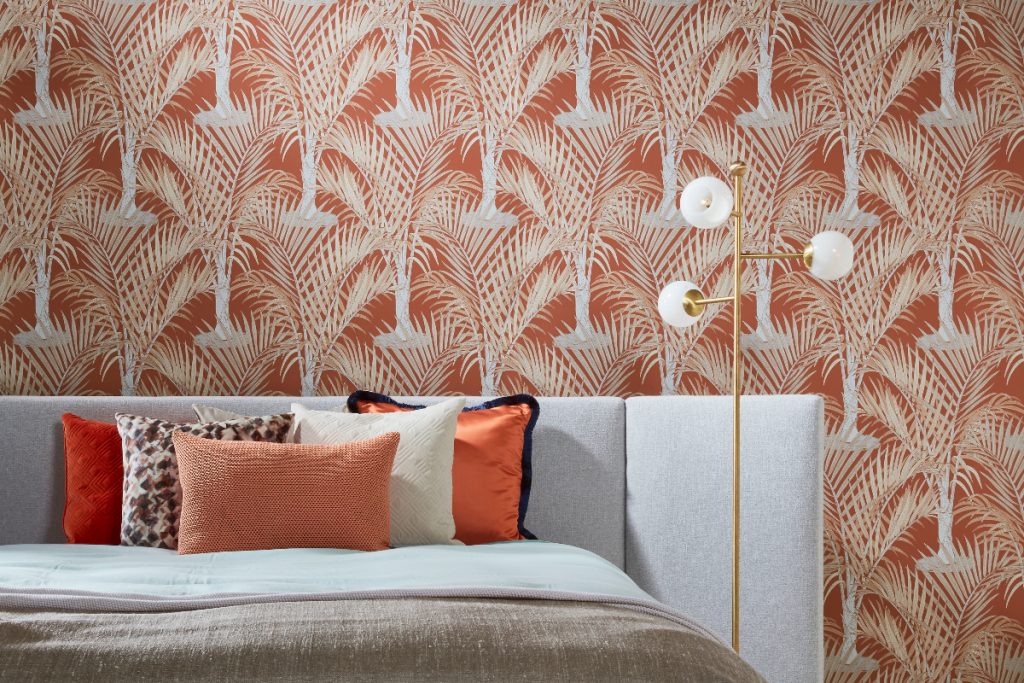 the latest wallpaper from Hooked on Walls in orange and white shades featuring palm trees, behind a light grey double bed with orange and brown bedding