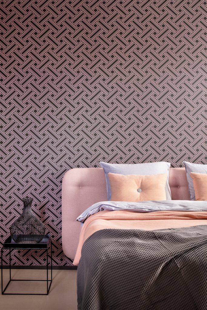the latest wallpaper from Hooked on Walls in a purple and black print behind a pink double bed with peach and grey bedding