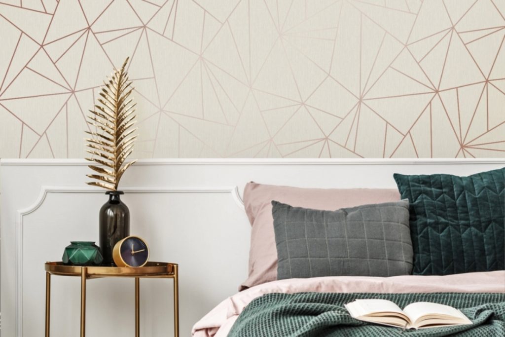 a geometrical gold and beige print behind a pink and green double bed with a brass bedside table