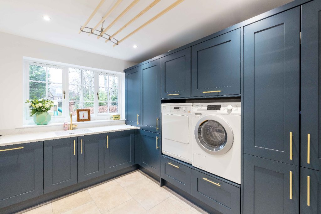 a utility room with brass handles on navy cabinetry that matches the blue shaker-style kitchen