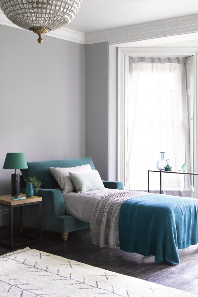 a teal sofa bed with purple and blue bedding in a large room with a chandelier