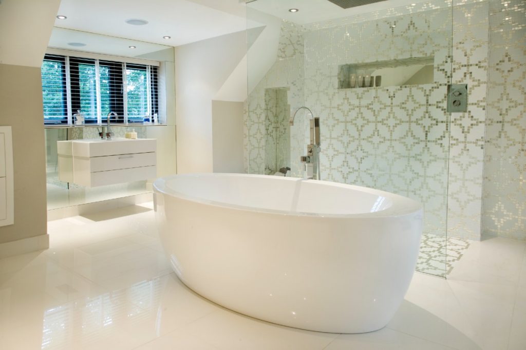 a white freestanding oval tub in a large bathroom with a large walk-in shower with gold geometrical wall tiles 