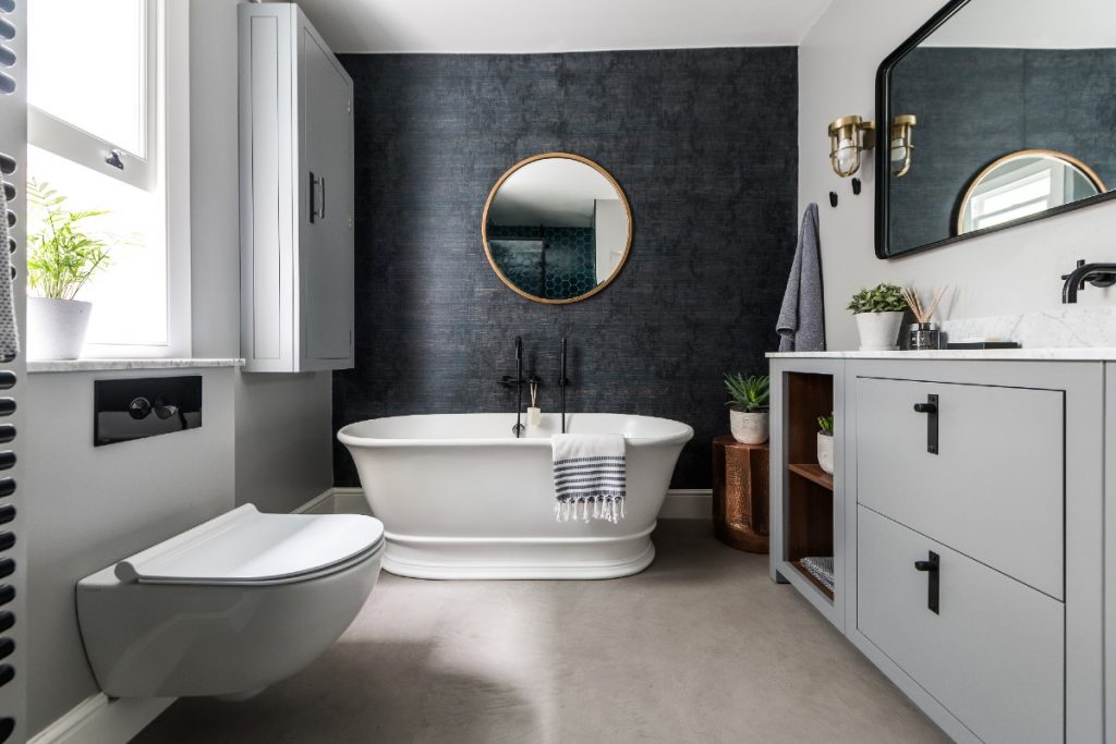 a traditional round white double‐ended bath in a grey bathroom with matt black fittings