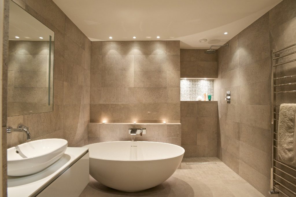 a round freestanding tub with a wall-mounted chrome tap in a neutral stone-coloured bathroom