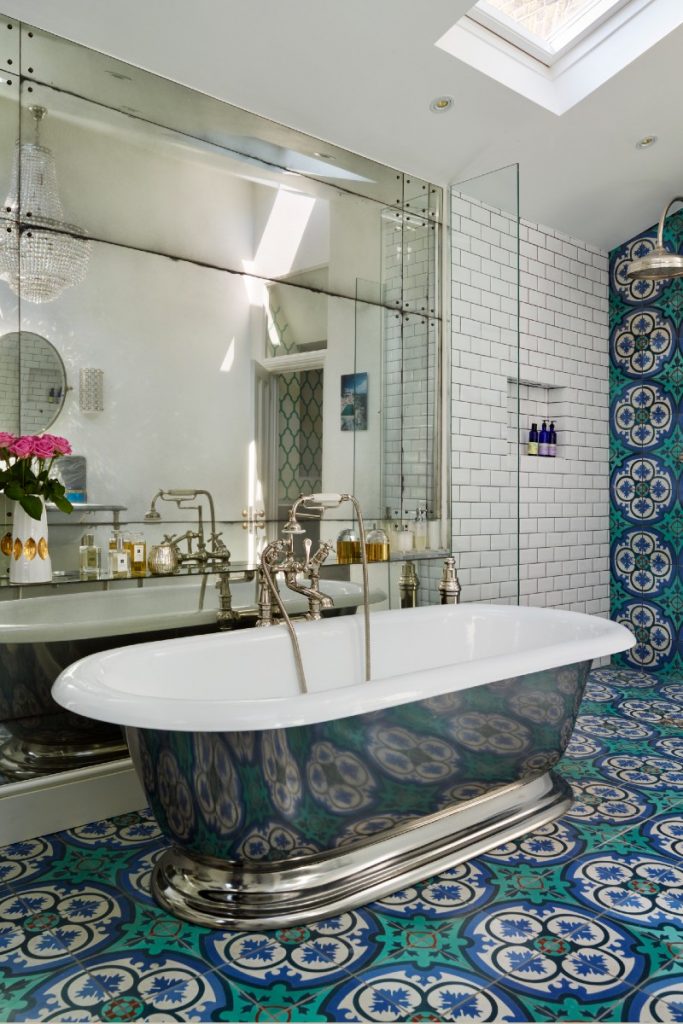 a double‐ended bath in a bathroom featuring geometrical floral blue and green tiles and a large wall mirror