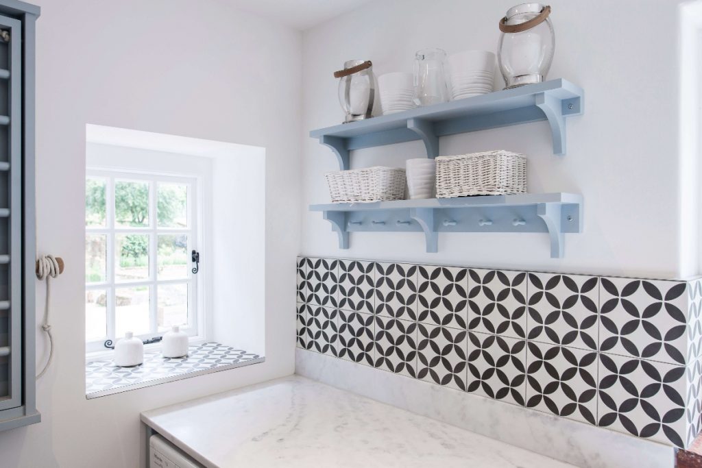 pale blue shelves with storage baskets and tube on them above a kitchen worktop with geometrical tiles