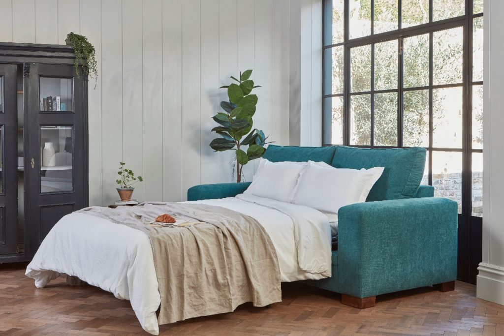 the Darlings of Chelsea Ashdown bed in teal next to a large plant in front of a brown window 