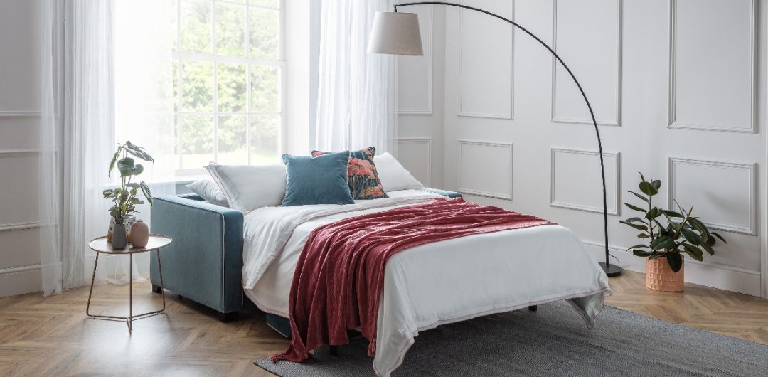 a double sofa bed with teal and floral cushions and an arc floor lamp with a grey shade