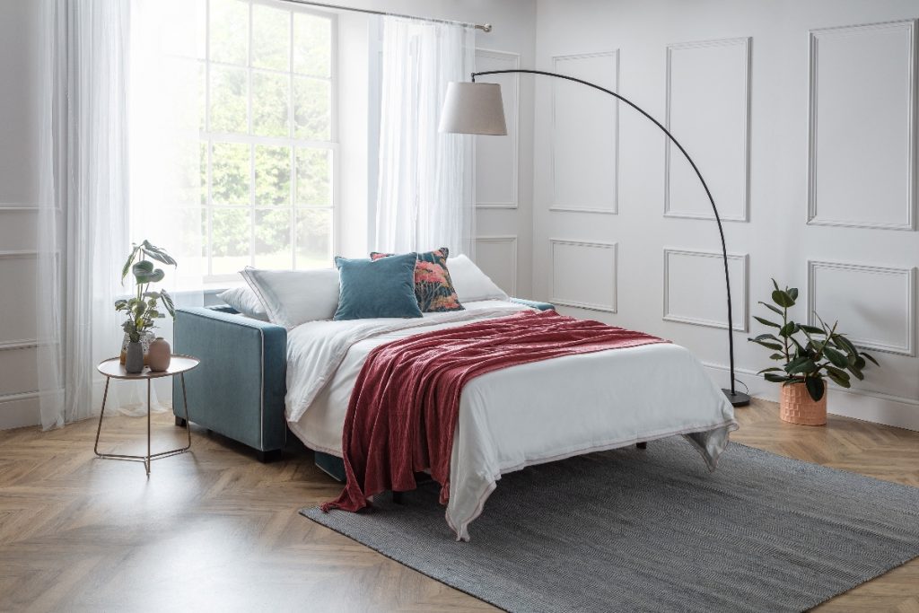 the Furl duette model with a red throw, floral cushions, an arc lamp and several plants in a spacious bedroom with a grey rug and white wall panelling