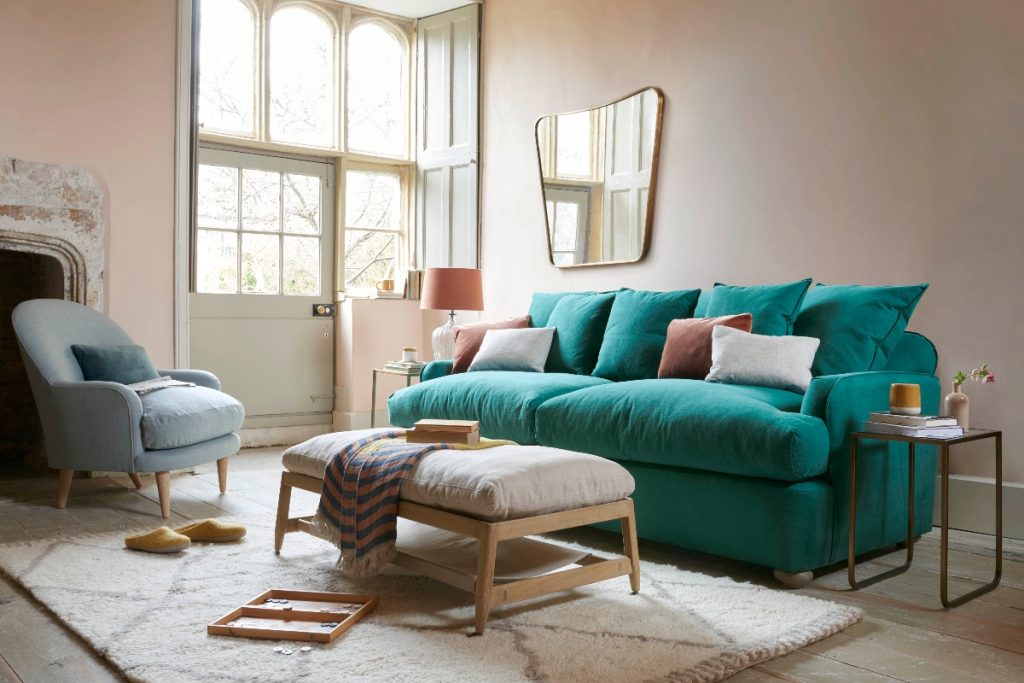 the Loaf Indian Green brushed cotton sofa with orange and white cushions and a wooden table with a beige cushion