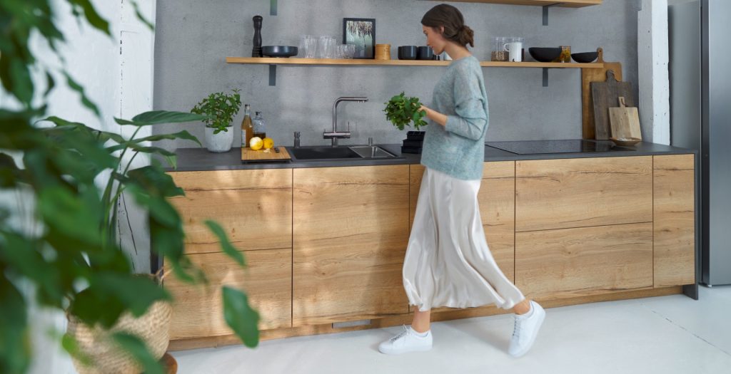 a woman carrying herbs to the sink in a wooden kitchen with a charcoal grey worktop 