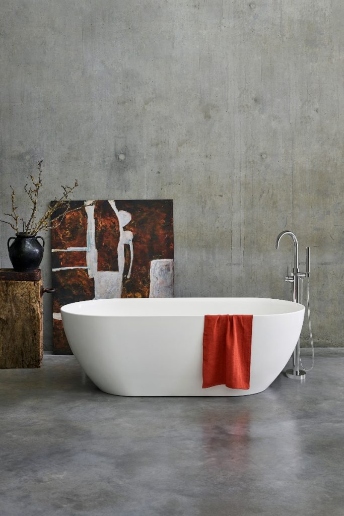 a freestanding white compact bath in a grey bathroom with a red towel, a chrome tap and a painting behind them