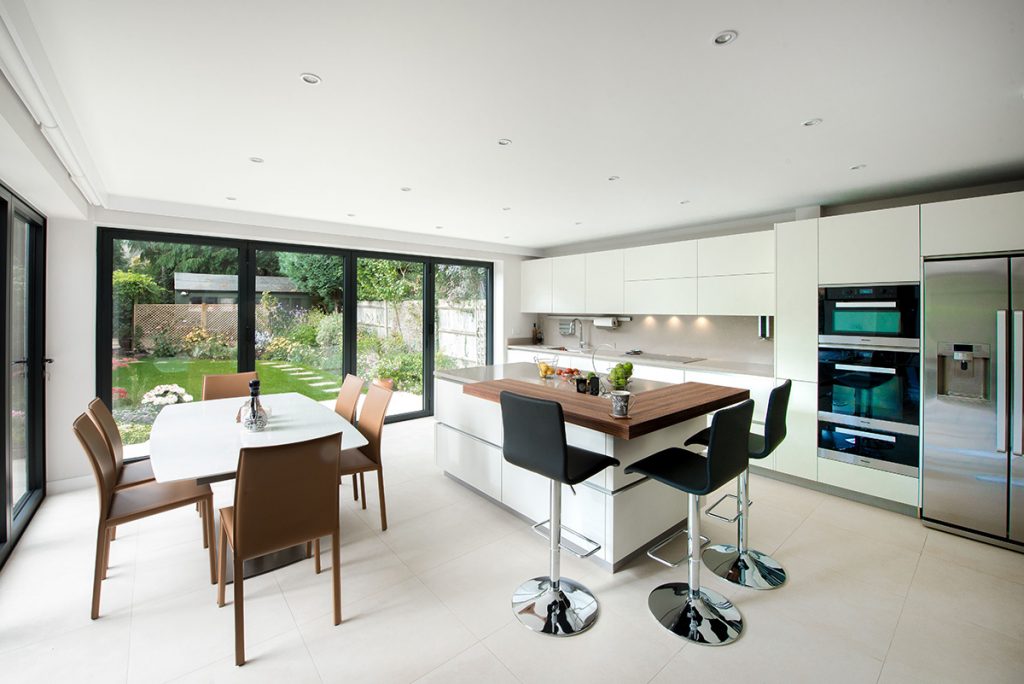 a double‐storey renovation featuring a kitchen island with three black bar stools around it and a dining table with chairs around it