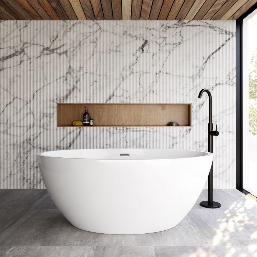 a freestanding white compact bath in a marble bathroom with a black tap and toiletries and accessories 