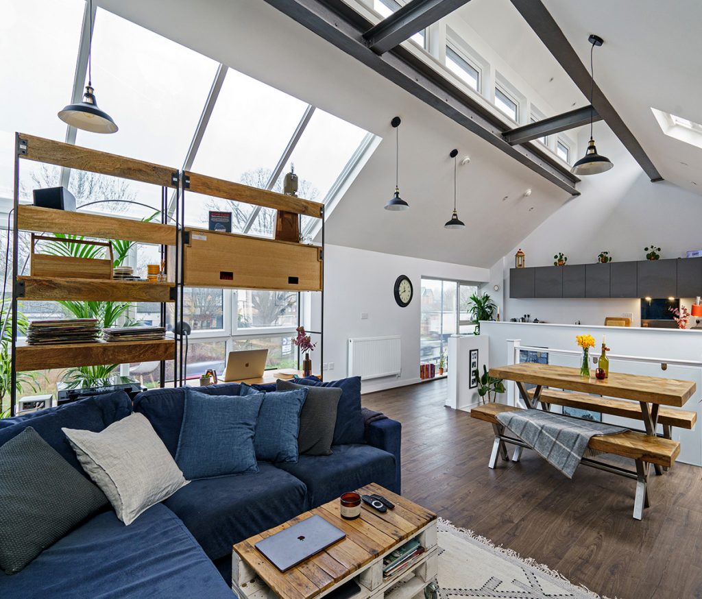 a kitchen diner featuring a navy corner sofa, wooden bench, wooden shelving unit and grey cabinetry