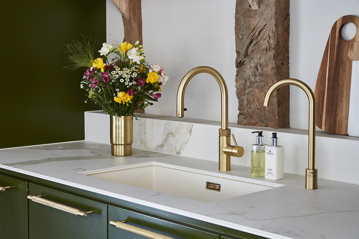 a pair of brass taps above a white undercounted sink next to a bunch of colourful flowers in a brass vase