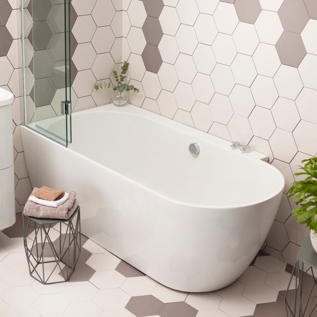 a freestanding white compact bath in a beige bathroom with hexagonal tiles, toiletries and accessories 