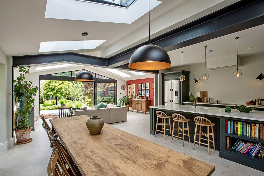 a kitchen extension with black pendant lights hanging over a wooden dining table