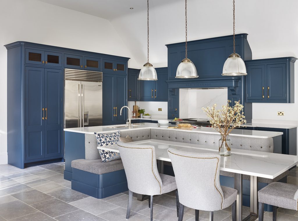 a navy kitchen with grey banquette seating and grey dining chairs with brass trims