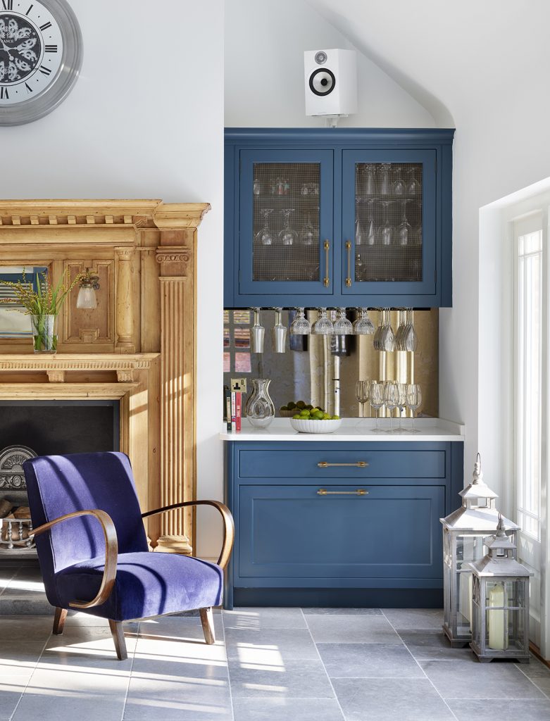 a fluted glass drinks cabinet painted navy with brass handles and lots of glasses inside it