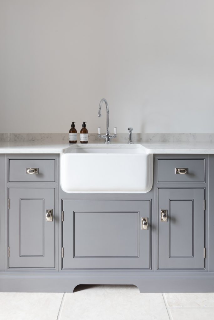 a white Belfast sink with a chrome tap set in grey cabinetry with chrome handles