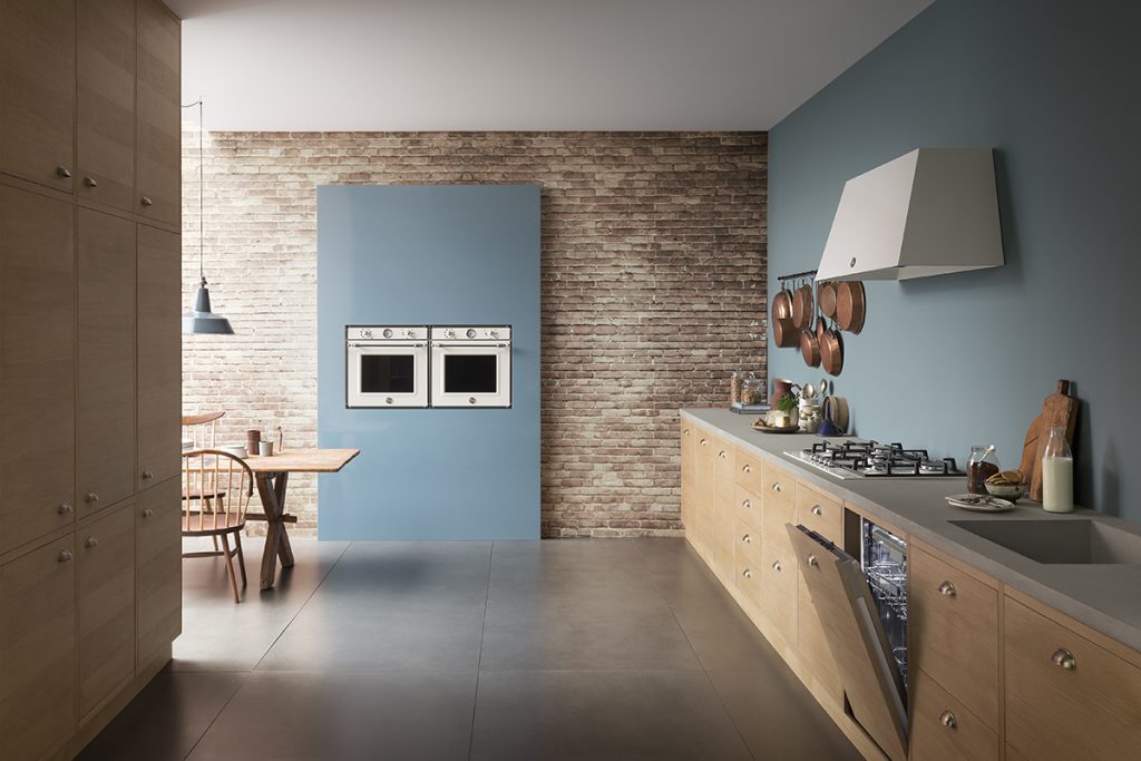 built-in appliances in a blue wall against exposed brickwork in a kitchen with wooden cabinetry with chrome cup handles
