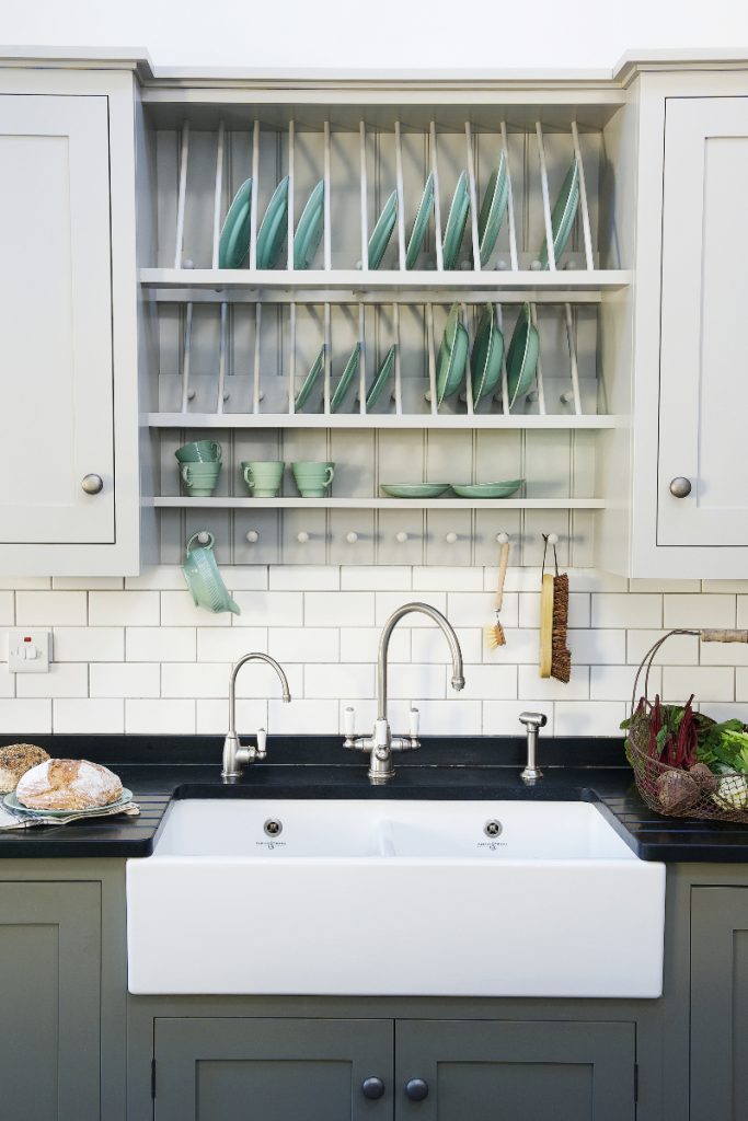 a white Belfast sink with silver tap and white metro tiles above it under hooks and shelves with sea green crockery