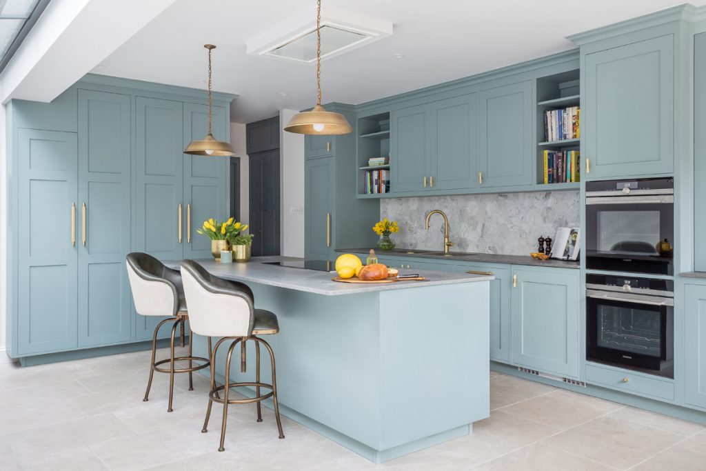 a pale blue kitchen with Shaker cabinetry and brass handles and pendant lights