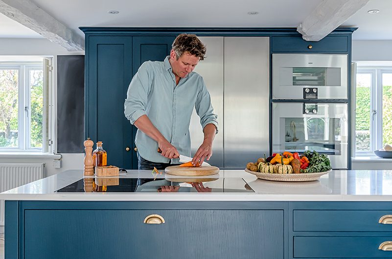 a man preparing food at an island with navy cabinetry with brass cup handles