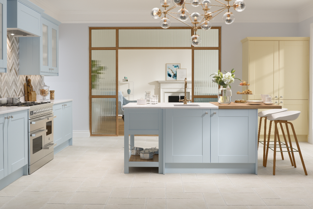 a pale blue Shaker kitchen with a central island and two white and wooden bar stools against it