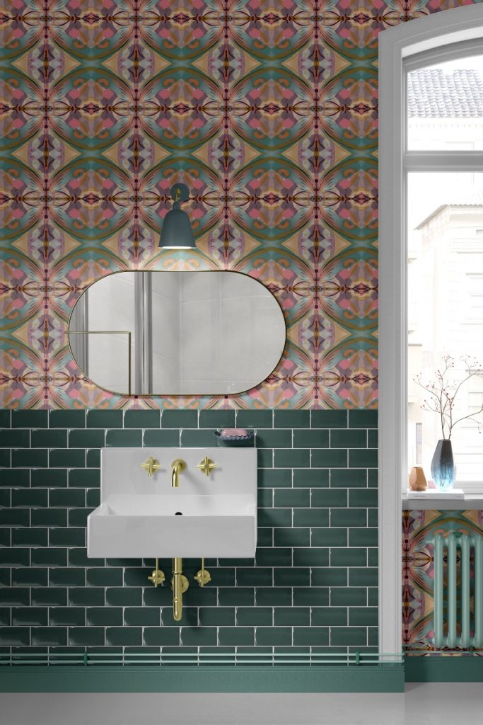 a geometrical design above green metro tiles, a white ceramic sink and brass taps