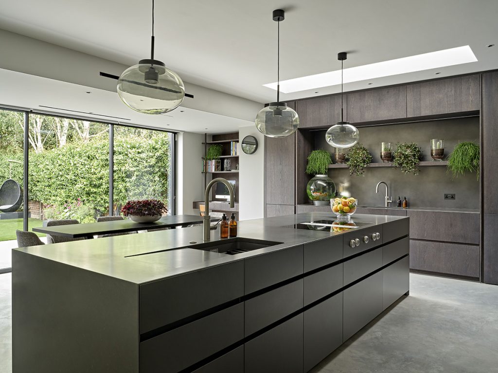 a dark open plan kitchen featuring dark wood and a large forest green kitchen island with three pendant lights hanging above it