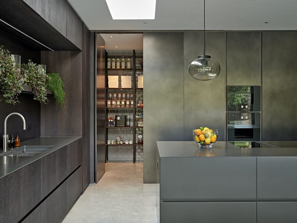 a dark kitchen featuring an open pantry cupboard fully stocked with groceries
