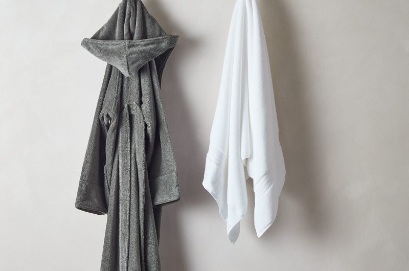 a guest bathroom robe in grey with a stack of towels on a bench in grey, white and beige