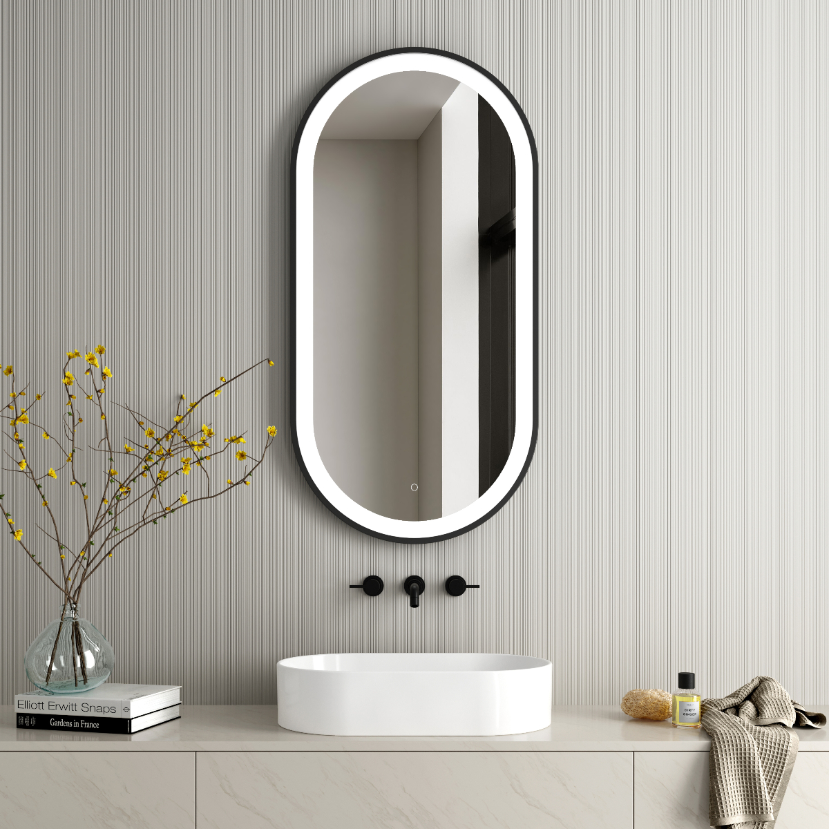 an illuminated round LED mirror in a guest bathroom with a white countertop basin, matt black hardware, beige cabinetry and accessories