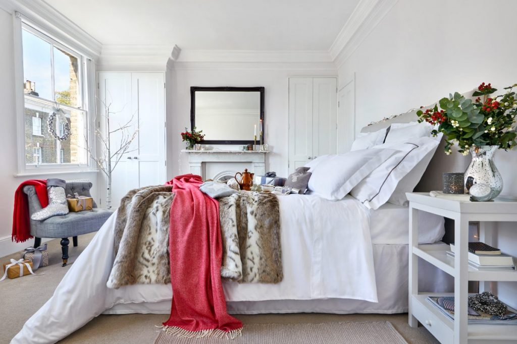 Pared-back bedroom with white bedding, red throw and bedside table decorations