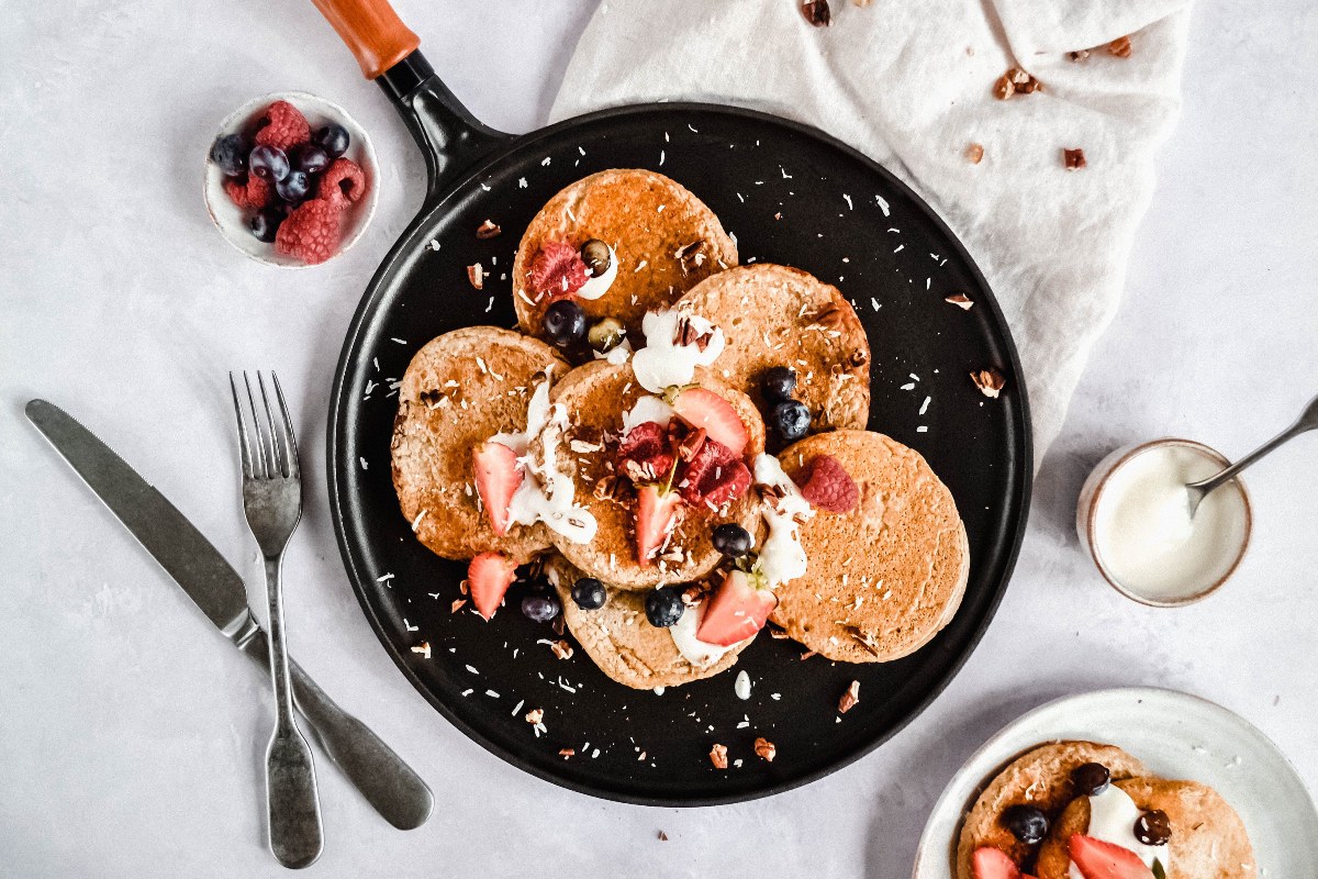 Delicious, sweet pancakes with fruits pictured on cookware with a wooden handle